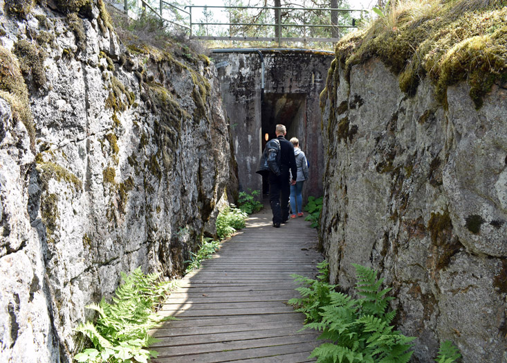 Matkailijoita kävelemässä kallioon louhittua yhteyshautaa pitkin betonikorsuun.